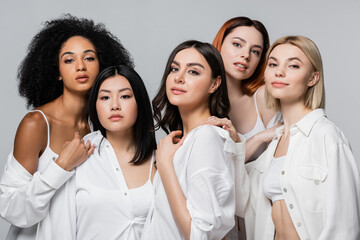 asian and curly african american models in white shirts posing with women isolated on grey