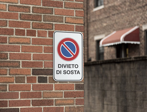 Cartello stradale divieto di sosta su strada con muro in mattoni rossi.