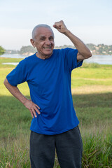 portrait of an active and happy senior man excited and celebrating with hand up outside on a sunny day