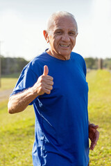 portrait of a senior man doing thumbs up and looking to camera in a park on a sunny day
