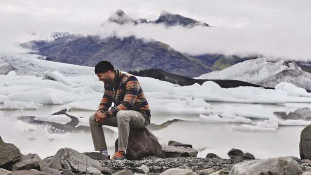 Male Tourist Sitting on Rock While Posing for Photo with Glacier in Background
