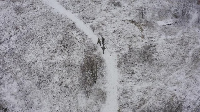 Threesoldiers in full uniforms go to the places of hostilities in winter. aerial view