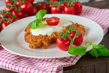 Schnitzel with melted mozzarells cheese, tomatoes and basil on a plate