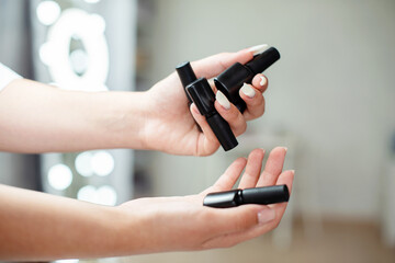 Female hands holding bottles of nail polish at beauty salon, close up with copy space, background with lights, nail polish presentation for manicure blog, online manicure course