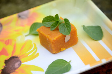 closeup the yellow gram flour sweet with green mint over out of focus white brown background.