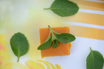 closeup the yellow gram flour sweet with green mint over out of focus white brown background.