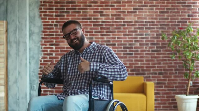 Happy cheerful bearded disabled man with glasses is sitting in wheelchair, dancing and rejoicing , front view. Hipster is not discouraged and enjoys life. Concept of accepting yourself, your diagnosis