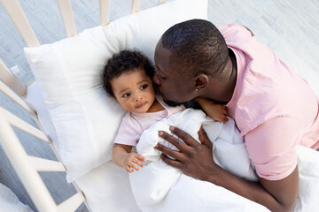 african-American dad kisses and hugs baby son in crib before going to bed