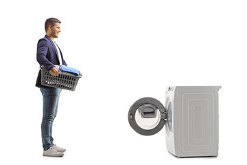 Full length profile shot of a man with a laundry basket standing in front of a washing machine - obrazy, fototapety, plakaty