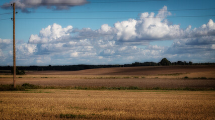 glowy moody Latvian summer scene with cloudy blue sky, agricultural field after harvesting,...