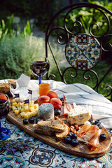 Cheese platter with different cow and goat cheeses, meat, nuts, Summer fruits and berries, jam and rye bread on wooden board.with red wine on little rustic table in the garden.