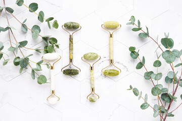 Jade face rollers and eucalyptus branches on a white marble background. SPA concept. Top view, copy space