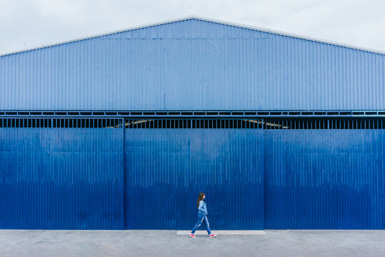 Woman walking along blue building in city