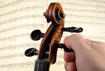 Naklejka premium Violinist tunes a violin against the background of open notes out of focus, close-up