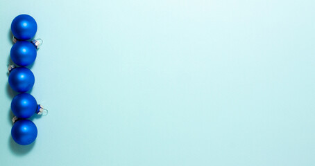 Blue Christmas balls on blue background on left side. Flat lay top view with copy space. Holidays concept