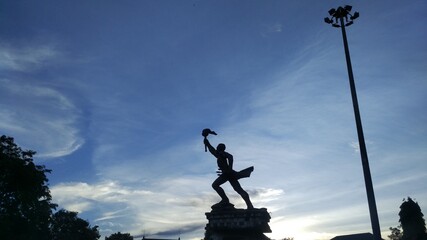 Torch-bearing man statue on a bright blue sky background
