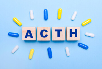 On a light blue background, multicolored pills and wooden cubes with the text ACTH. Medical concept