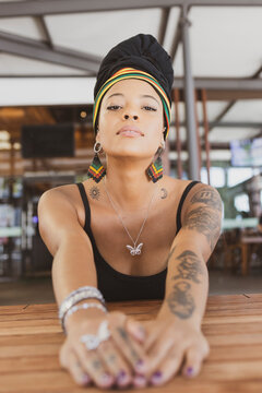 Beautiful tattooed African American woman wearing an african turban sitting at the table with arms outstretched looking at the camera with a hidden smile. Copy space for text.