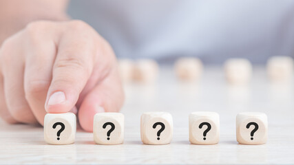 Male fingers pointing wooden cube blocks with question marks. ? Questions Mark words in wooden cube blocks on table background.