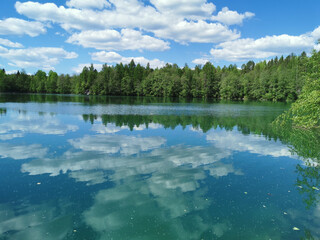 Fototapeta premium The shore of the lake is bright with clear water, in which you can see the marble on the bottom and reflect the sky with clouds, in the mountain park Ruskeala.