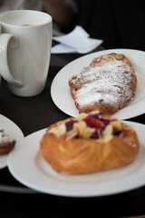 an almond croissant and a bun with strawberry slices lie on a white plate next to a white cup of coffee cappuccino and latte food fresh pastries bakery handmade kitchen cafe breakfast health
