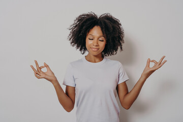 Calm and peaceful young mixed race woman keeping hands in mudra gesture and eyes closed