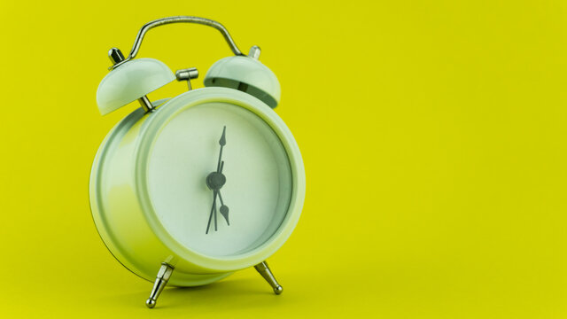White alarm clock on yellow table background.