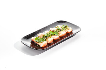 Salmon tataki - seared salmon, thinly sliced sashimi style. Salmon tataki served with delicious citrus ponzu tataki sauce and fresh greens. Japanese seafood on black plate isolated on white