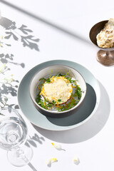 Beef tartare under cheese sauce with deep fried onion. Fancy dinning with beef tartare on white table with simple contemporary decoration. Sunlight and harsh shadow still life. Beef tartare blue dish.