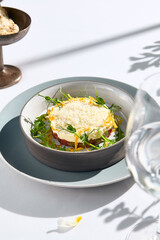 Beef tartare under cheese sauce with deep fried onion. Fancy dinning with beef tartare on white table with simple contemporary decoration. Sunlight and harsh shadow still life. Beef tartare blue dish.