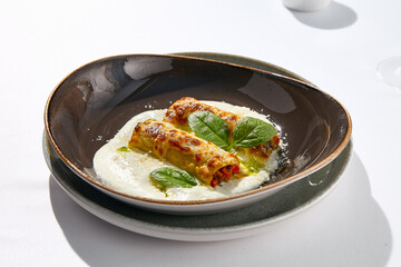 Italian beef cannelloni with bolognese ragu, bechamel sauce and cheese. Baked pasta cannelloni with meat and cheese parmesan. Italian aesthetic white table. Harsh shadow in Italian menu restaurant.