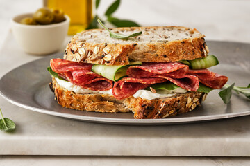 Sandwich with salami sausage and cucumber on marble background.