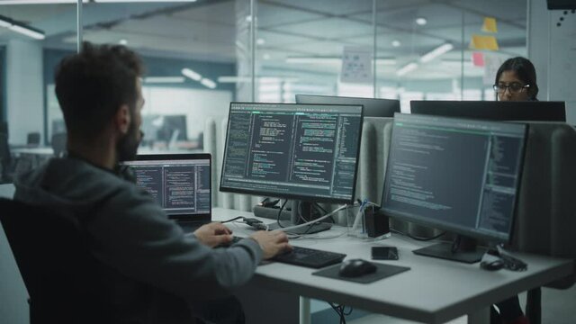 Diverse Office: IT Programmer Working on Desktop Computer. Male Specialist Creating Innovative Software Engineer Developing App, Program, Video Game. Terminal with Coding Language. Over Shoulder