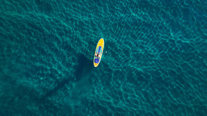 Aerial photo of man on sup board in clear blue sea