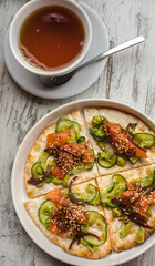 bread tortilla with salmon cucumber sauce and sesame along with tea on a white wooden background. healthy food background texture pita with red fish vegetables and sesame sprinkles. 