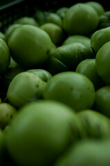 Green tomato (unripe) in wicker basket on wooden background. Unripe green tomato in bowl for fried dish or salted pickled vegetables. Raw green tomato on table for dinner