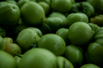 Green tomato (unripe) in wicker basket on wooden background. Unripe green tomato in bowl for fried dish or salted pickled vegetables. Raw green tomato on table for dinner