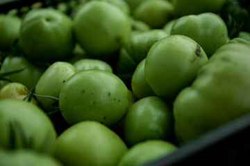 Green tomato (unripe) in wicker basket on wooden background. Unripe green tomato in bowl for fried dish or salted pickled vegetables. Raw green tomato on table for dinner