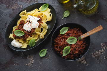 Top view of pappardelle with bolognese sauce and mozzarella cheese over brown stone background, horizontal shot