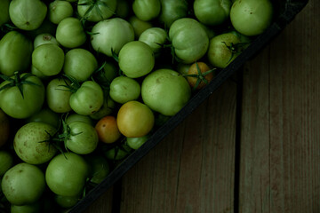 Green tomato (unripe) in wicker basket on wooden background. Unripe green tomato in bowl for fried dish or salted pickled vegetables. Raw green tomato on table for dinner