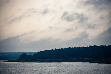 River landscape. Calm water and with clouds. Trees grow on the nearest shore. There is copy space