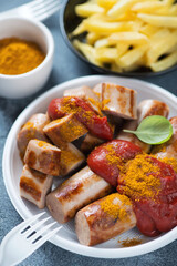 Currywurst or german traditional sausages served with tomato sauce and curry on a white plastic takeaway plate, close-up, vertical shot