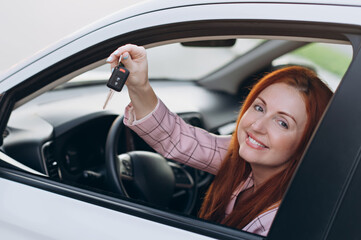 Woman bought first car. Joyful female sitting in new car and shows keys.