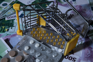 medicines and pills are lying in a small shopping cart against the background of money euro dollars...