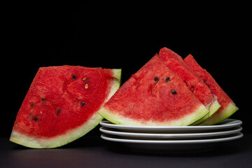 Sliced watermelon on a white plate on a black background. Slices of juicy watermelon