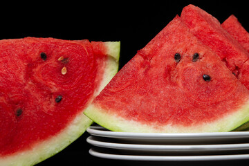 Sliced watermelon on a white plate on a black background. Slices of juicy watermelon