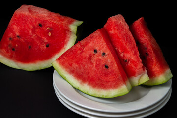 Sliced watermelon on a white plate on a black background. Slices of juicy watermelon