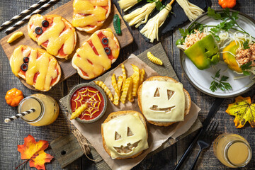 Halloween party food corner table scene over a wood background. Halloween party burger, mummies mini pizzas, halloween drink, Bell peppers with spaghetti and and minced tomato turkey. 