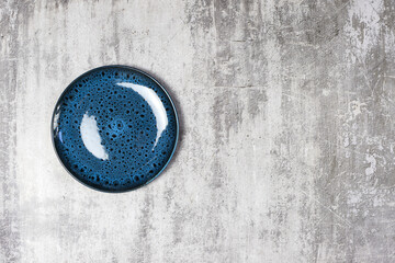 Top view of round blue plate with pattern on light cement background, copy space for your design.