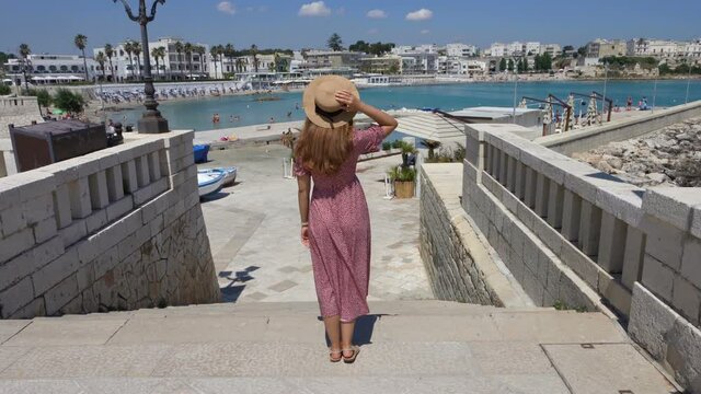 Tourist girl with dress and hat walking enjoying seascape in Otranto town, Salento, Italy